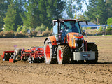 Red tractor with plow in a field with trees in the background